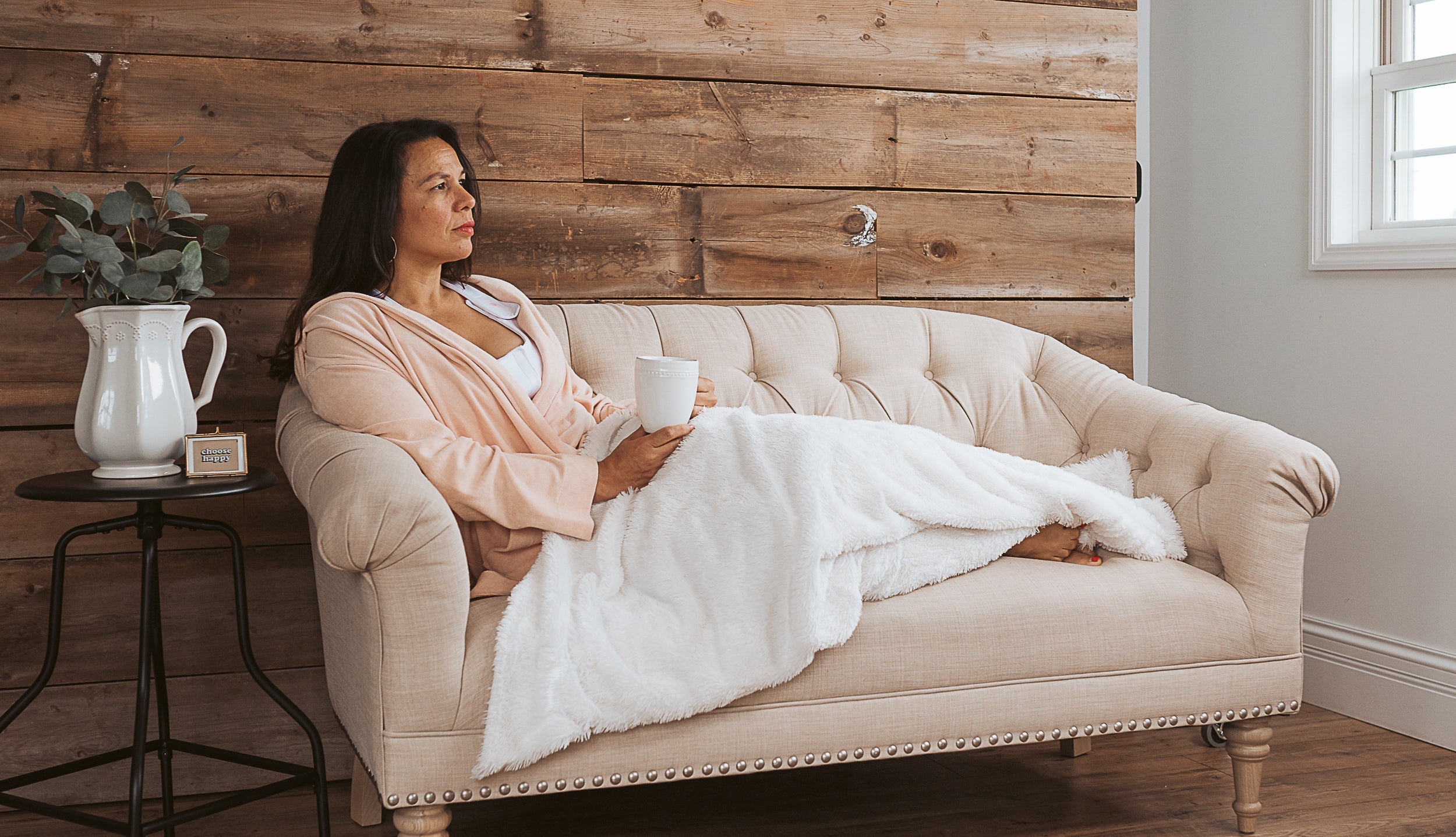A woman sits on a couch wearing a heart&core bra. Lear more about dressing for recovery after cancer surgery in our guide.
