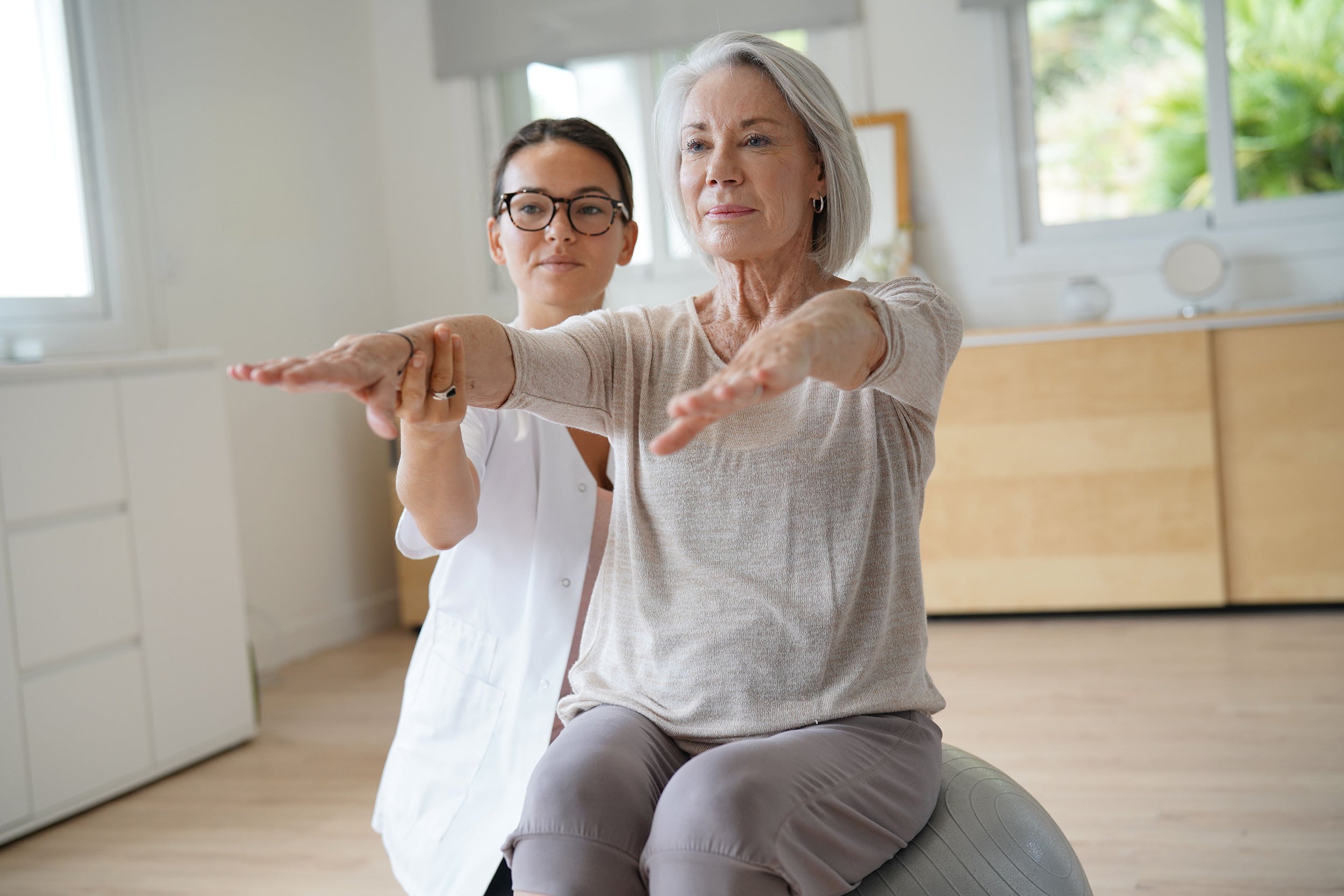 A senior woman works with a physical therapist. Front closure bras are a perfect solution for seniors with limited mobility. Learn more in our complete guide.