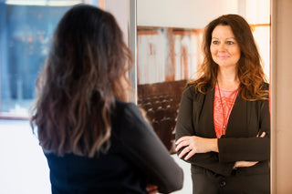 A woman looks at herself in the mirror. If you're facing liposuction recovery, learn more about which bra is right for you in our comprehensive guide on bras after liposuction.