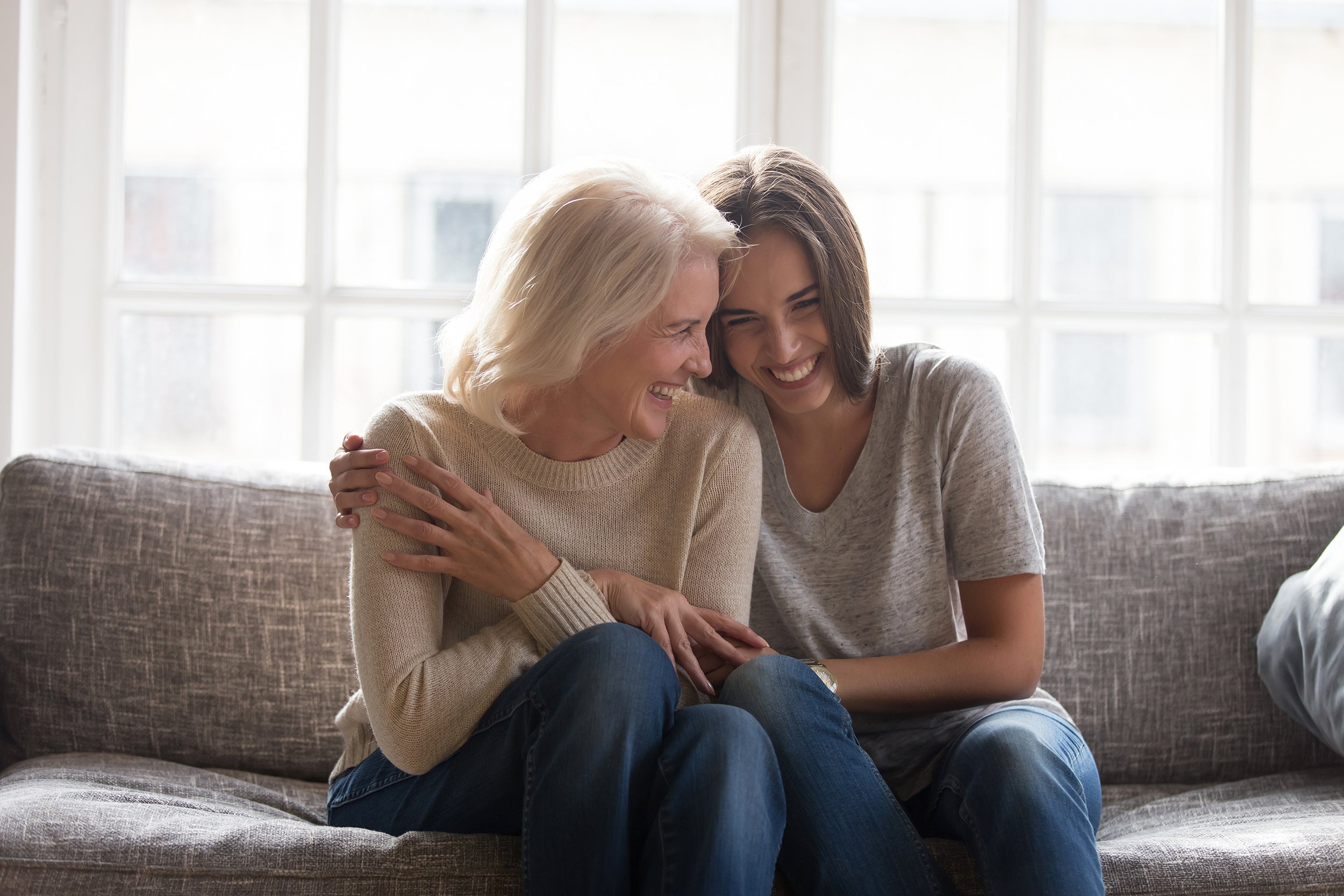 Two women hug while sitting together on a couch. Not all gifts for cancer patients are helpful. Discover which gifts are the worst gifts for breast cancer patients and what actually helps instead.