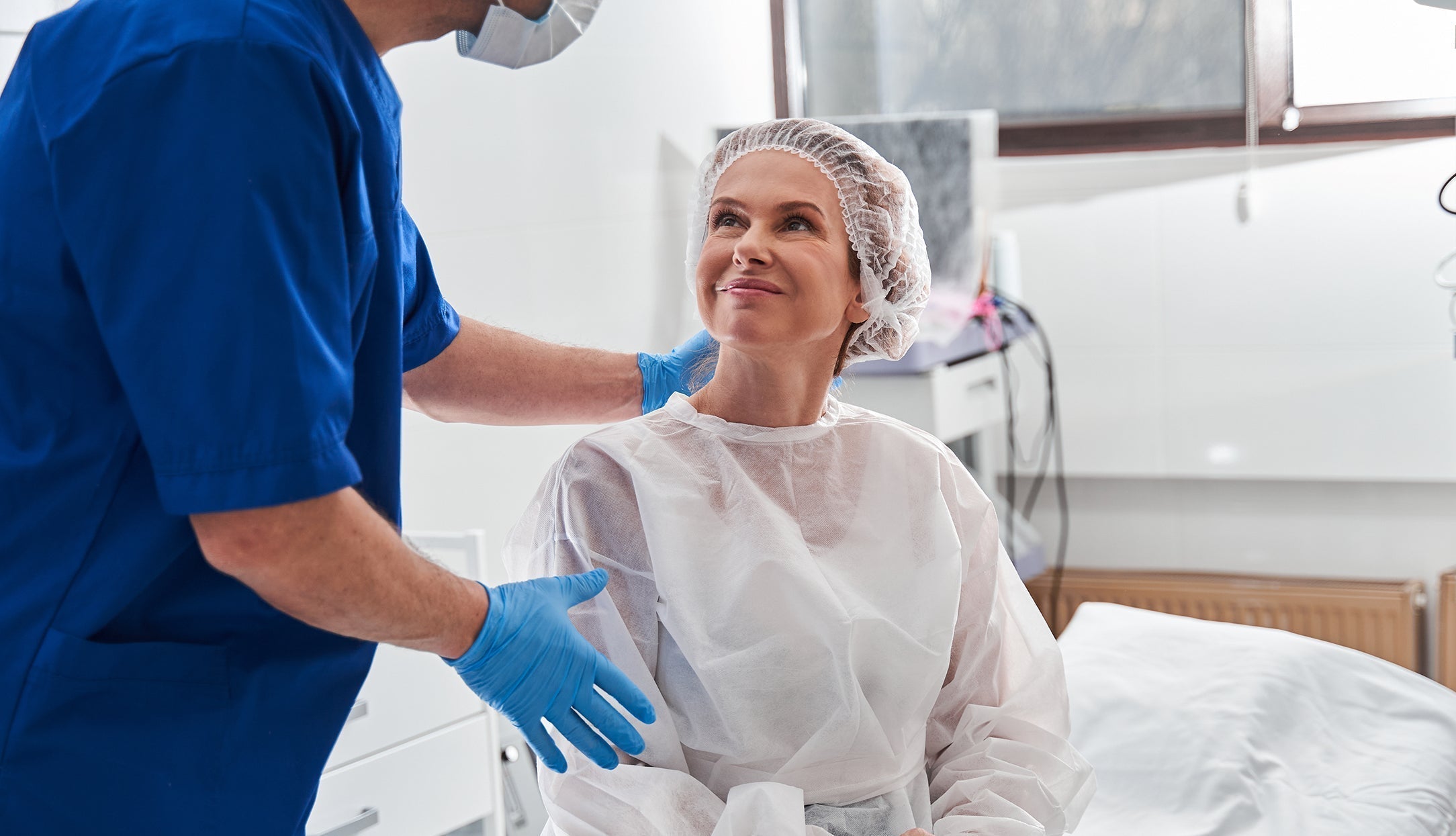 A woman talking to a doctor in a hospital gown. Learn what to wear after shoulder surgery in our complete guide.